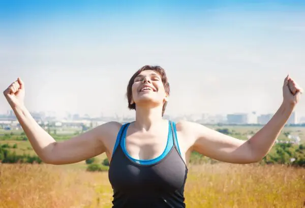 A woman standing in the grass with her arms outstretched.