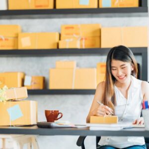 A woman sitting at a table with boxes in the background.