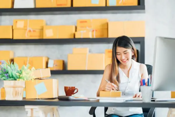 A woman sitting at a table with boxes in the background.