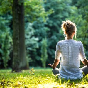 A woman sitting in the grass with her hands in yoga position.