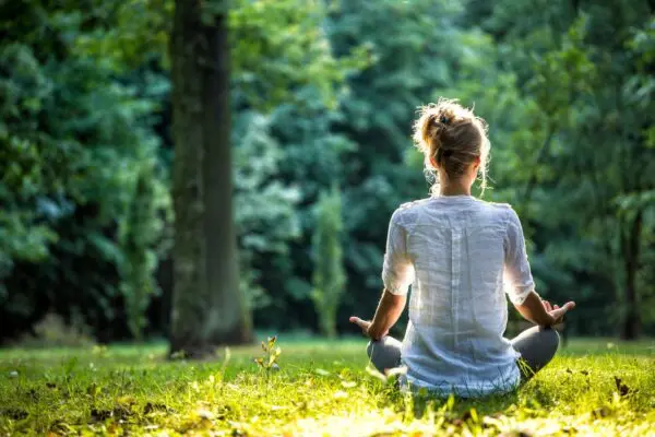 A woman sitting in the grass with her hands in yoga position.