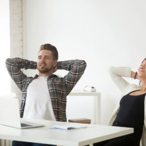 A man and woman sitting at a table with their hands behind their head.