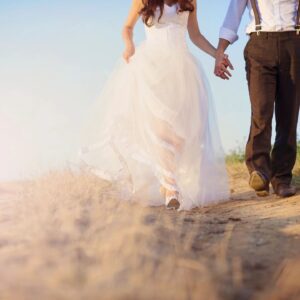 A bride and groom holding hands while walking in the sand.