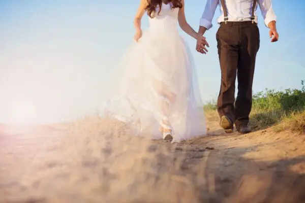 A bride and groom holding hands while walking in the sand.