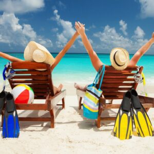 Two people sitting on a beach with their arms up.