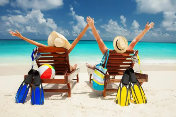 Two people sitting on a beach with their arms up.