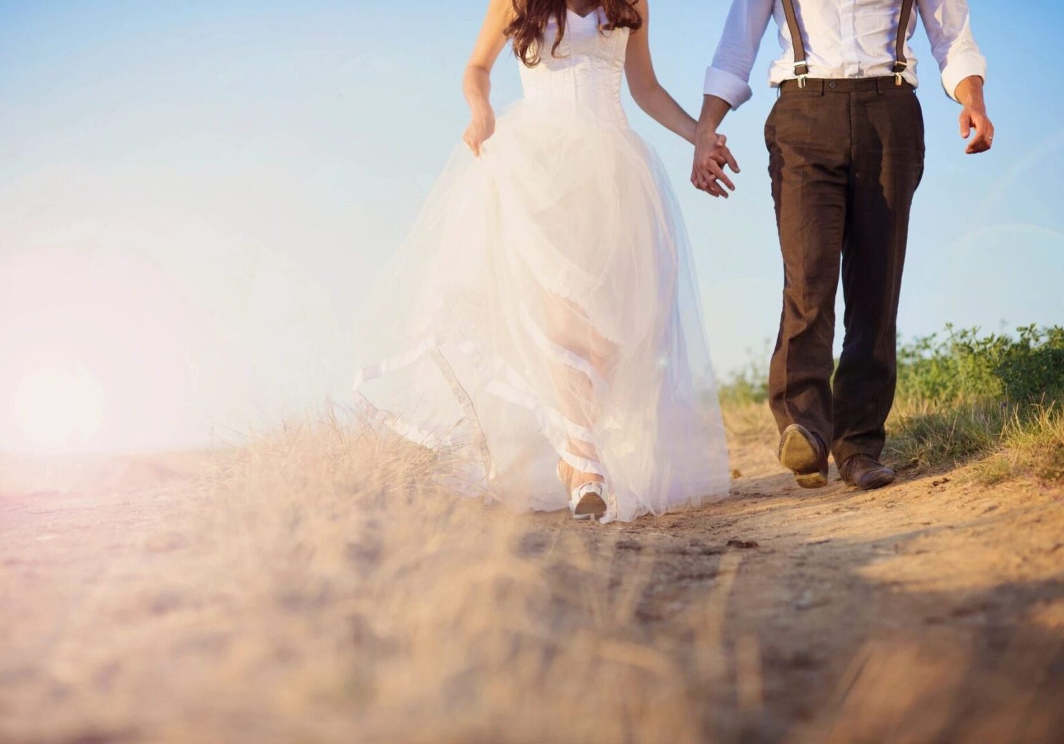 A bride and groom holding hands while walking in the sand.