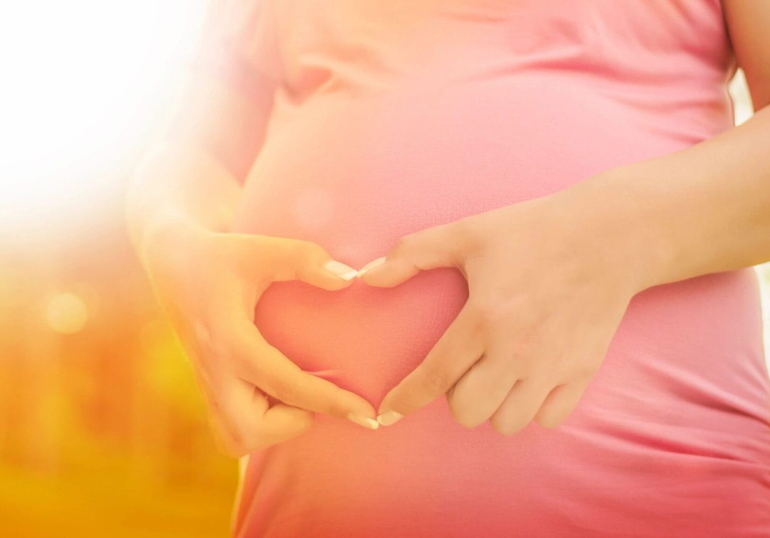 A woman holding her stomach in the shape of heart.