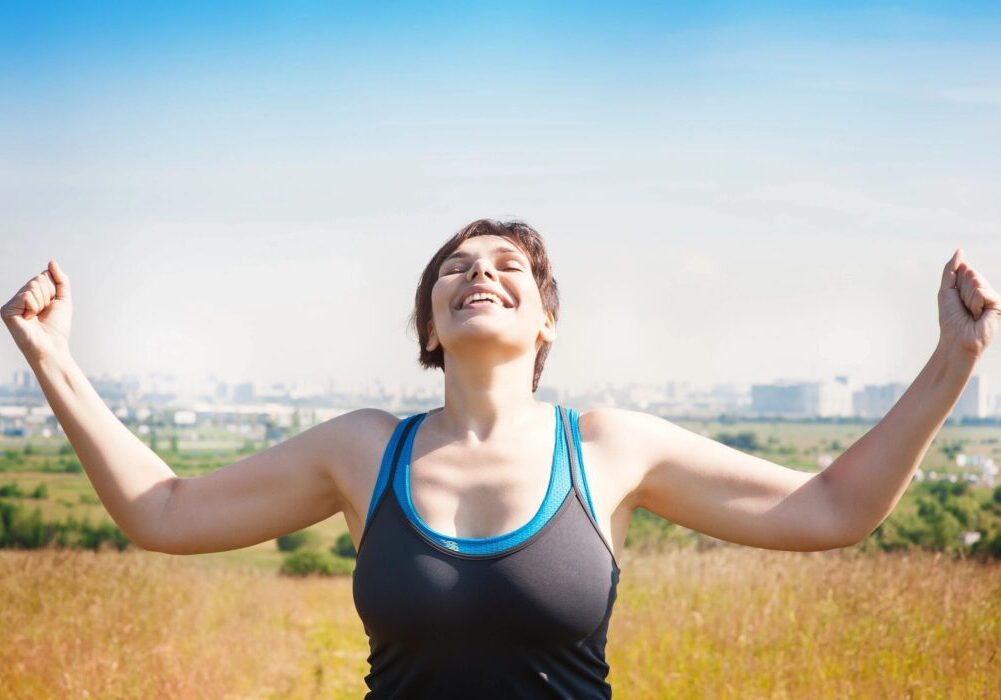 A woman standing in the grass with her arms outstretched.