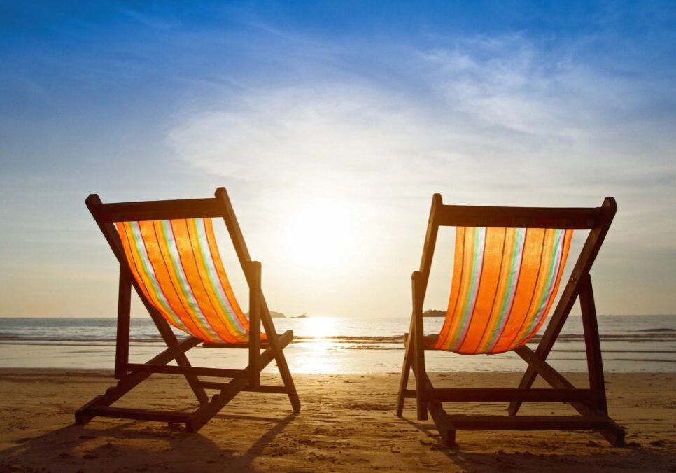 Two chairs on the beach facing each other at sunset.