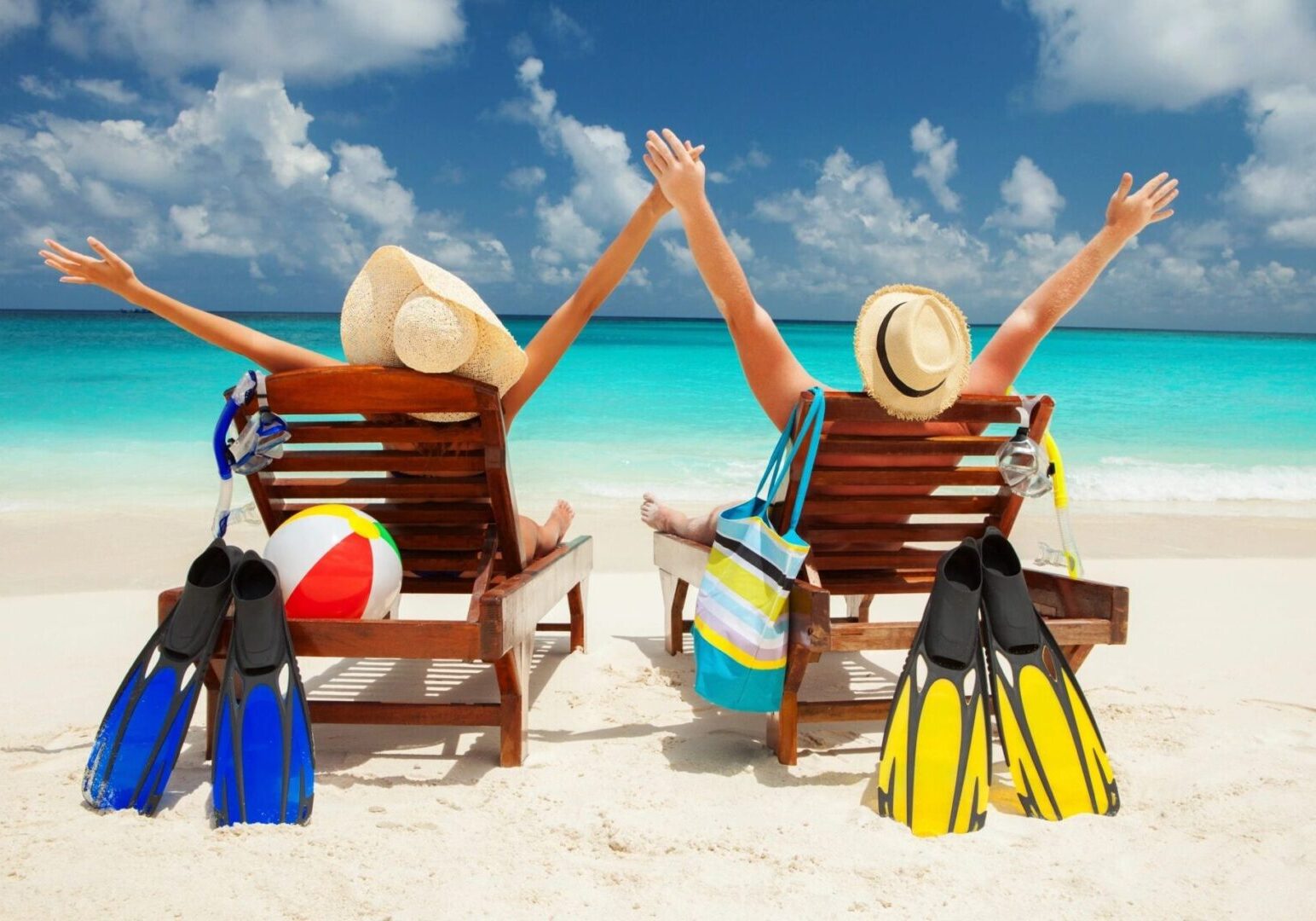 Two people sitting on a beach with their arms up.