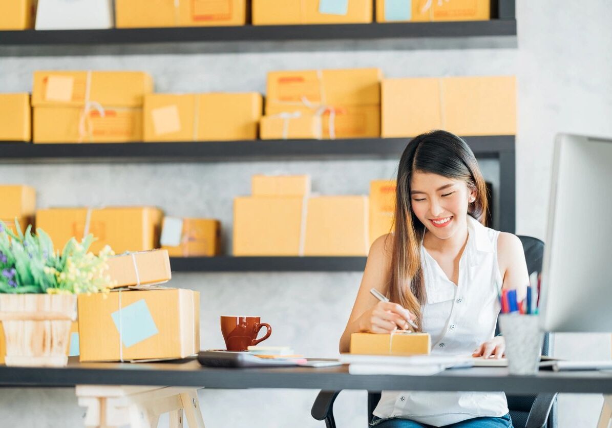 A woman sitting at a table with boxes in the background.