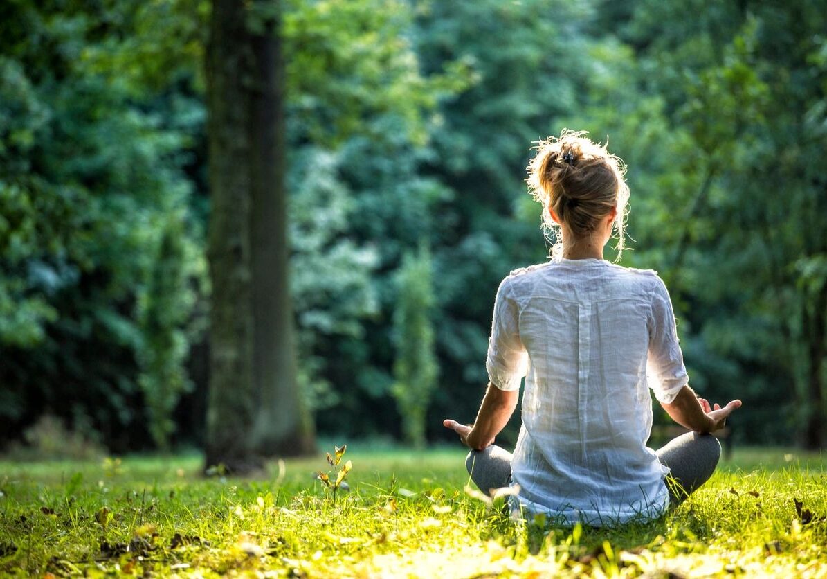 A woman sitting in the grass with her hands in yoga position.